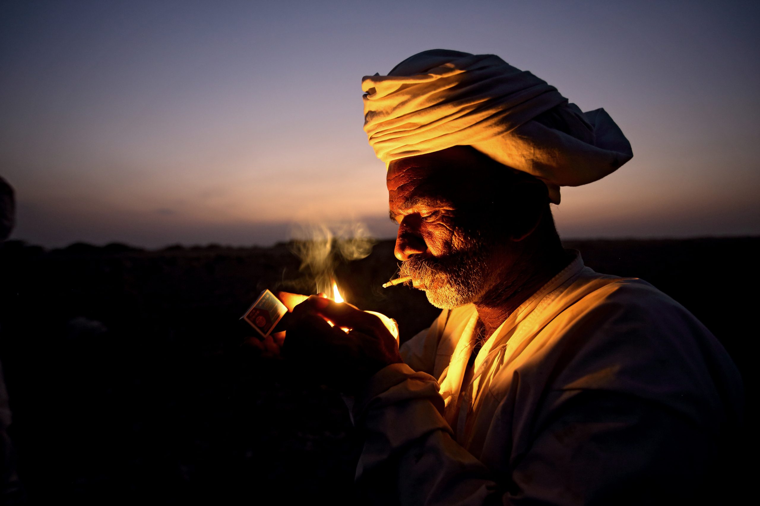 India-Gujarat. Abu Bai, il capo carovana del gruppo di famiglie Rabari Vagadiya, accende un beedi, o piccolo sigaro indiano. ph. Bruno Zanzottera©